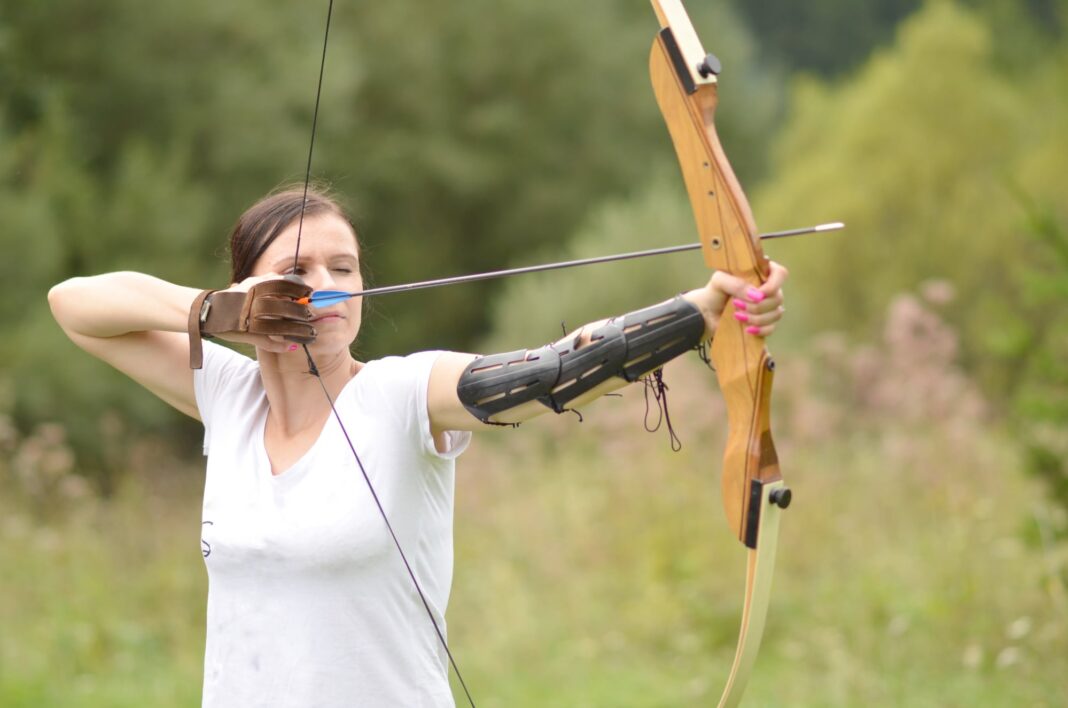 Persona practicando tiro con arco en un campo de tiro, enfocada en la postura y concentración.