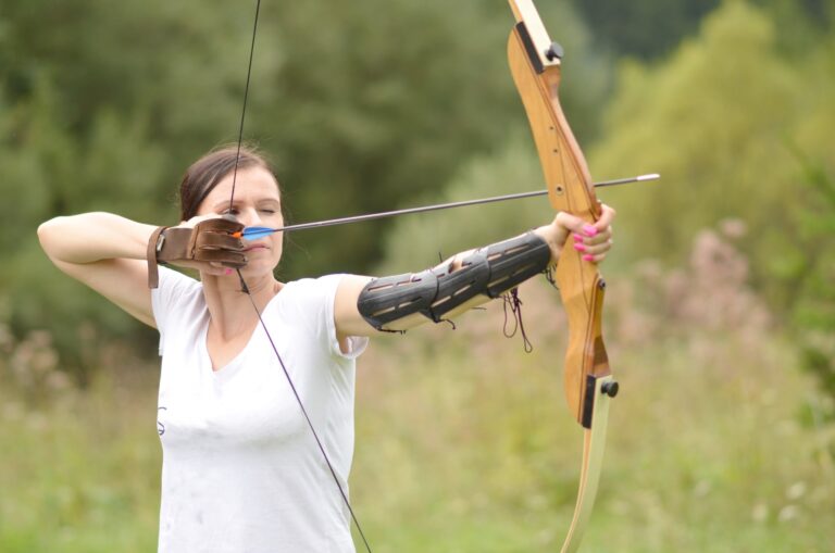Persona practicando tiro con arco en un campo de tiro, enfocada en la postura y concentración.