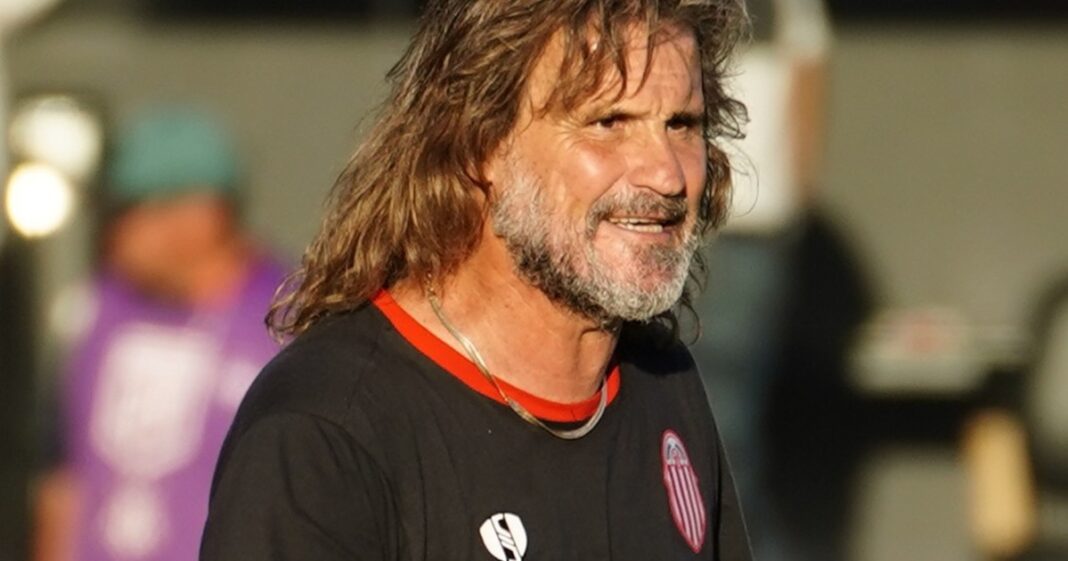 Escudos de Barracas Central y Sarmiento de Junín enfrentados en un partido de fútbol.