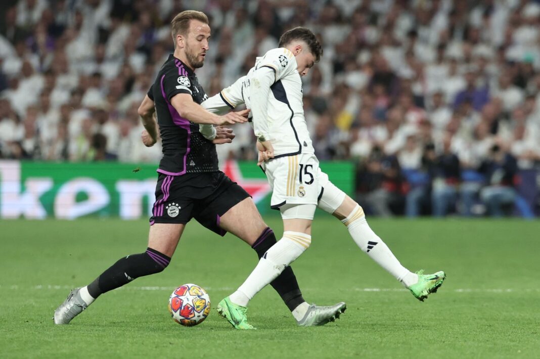 Escudos del Real Madrid y el Bayern Munich enfrentados, con el trofeo de la Champions League de fondo.