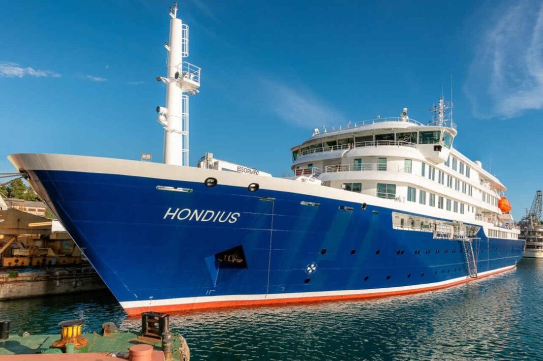 Crucero MV Hondius atracado en un puerto, con personal de salud y bandera neerlandesa