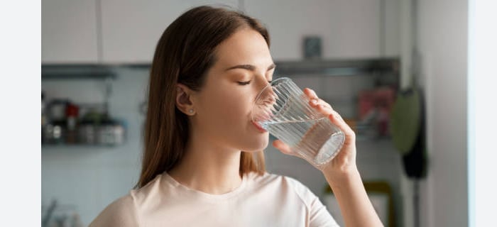 Mujer bebiendo un vaso de agua en la mesita de luz antes de dormir