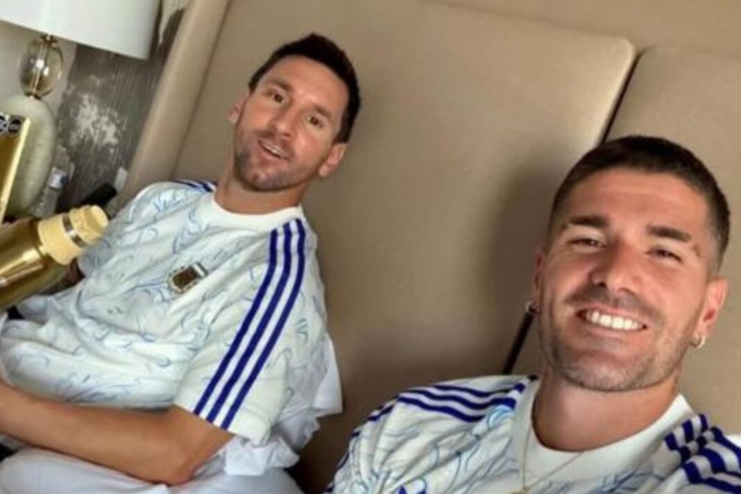 Selfie de Lionel Messi y Rodrigo De Paul en una cama, con Messi sosteniendo un termo dorado