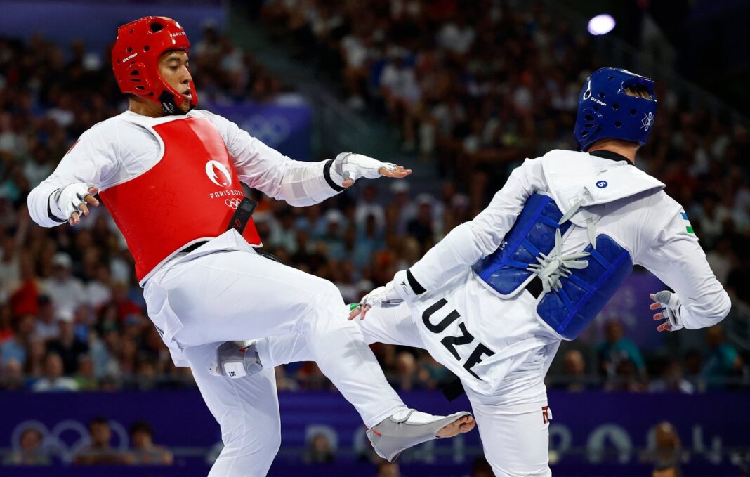 Atleta Cecilia Lee con dobok blanco y cinturón negro, bandera de México, realizando patada aérea en dojo con tapetes azules y rojos