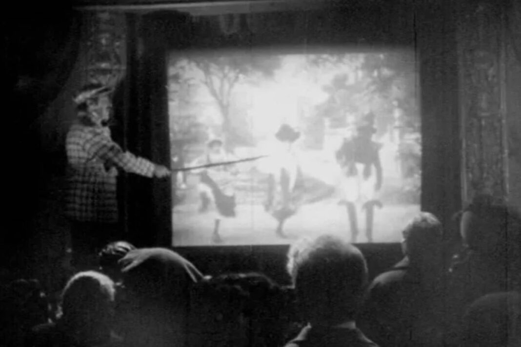 Sala de cine mudo con explicador señalando la pantalla