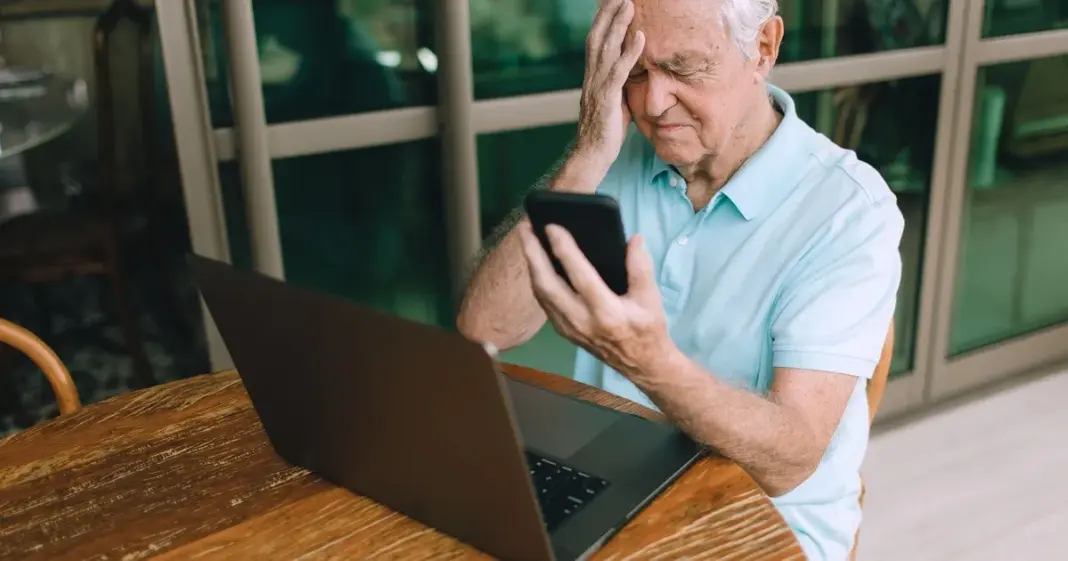 Persona usando un teléfono móvil y una computadora, ilustrando una posible estafa de suplantación de identidad