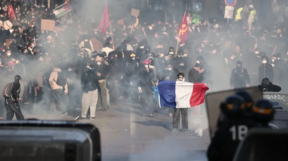 Personas manifestándose en una calle de París con carteles y banderas, y policías en la distancia